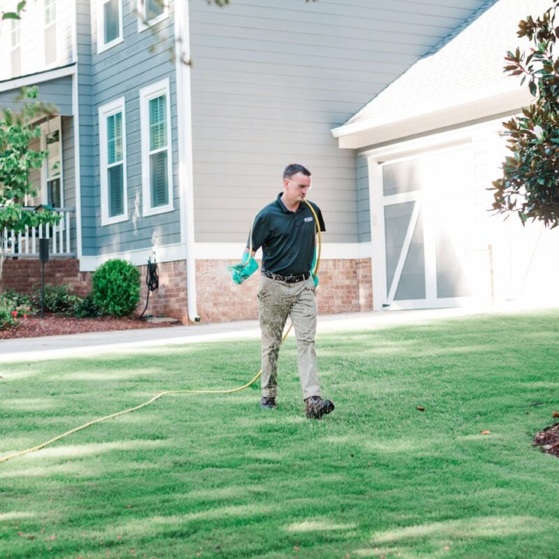 Nature's Turf employee treating turf with liquid aeration products on a lawn in front of a house