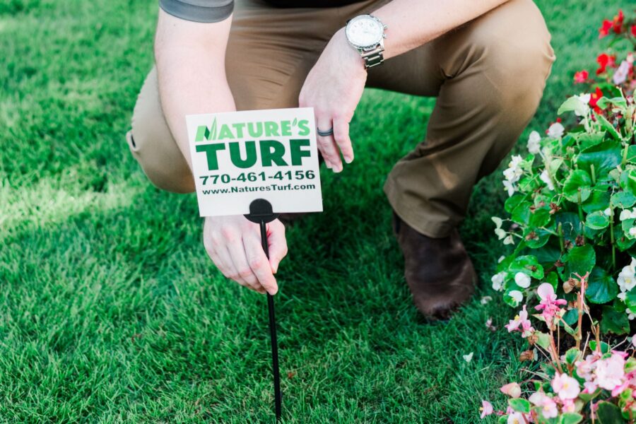 Nature's Turf employee planting a Nature's Turf yard sign in a lush green lawn next to flowers