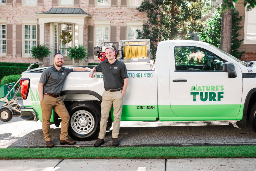 Nature's Turf employees standing by Nature's Turf truck in front of a brick house with a lush, green lawn