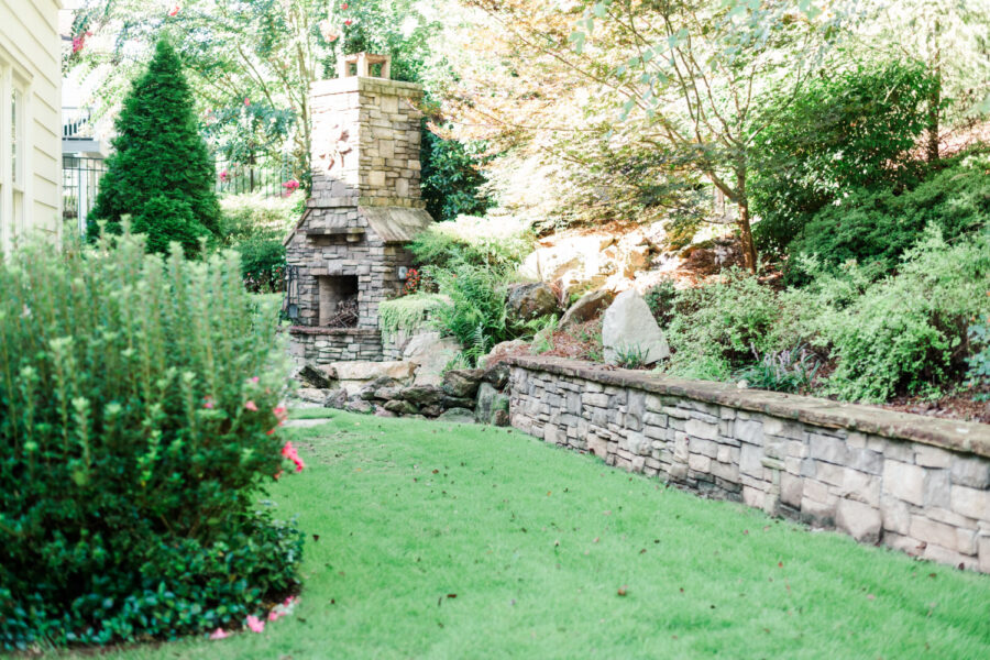 Outdoor fire place surrounded by a lush lawn, trees, and shrubs