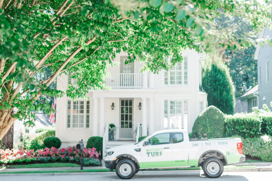 Nature's Turf truck parked on street in front of stately white house with a beautiful lawn full of flowers, shrubs, and trees