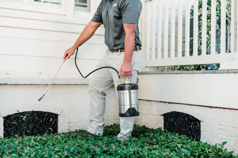Nature's Turf employee spraying pest control product around base of home