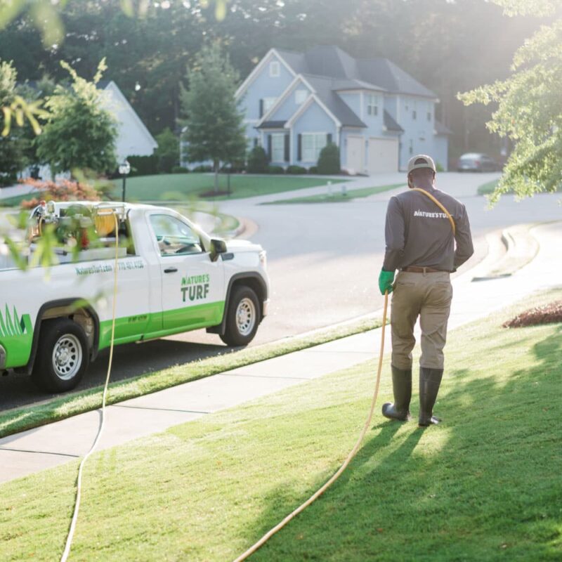 Nature's Turf employee applying weed control products to a lush green lawn beside a Nature's Turf truck