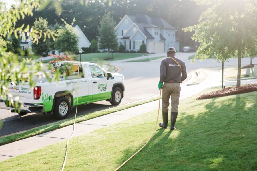 Nature's Turf employee applying weed control products to a lush green lawn beside a Nature's Turf truck
