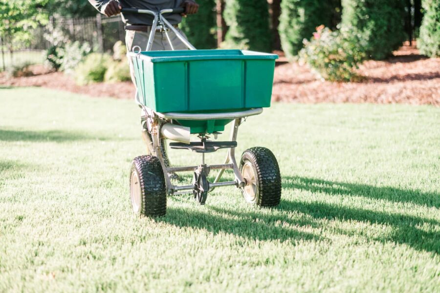 Nature's Turf employee applying limestone to a green lawn using a lawn product wheelbarrow applicator