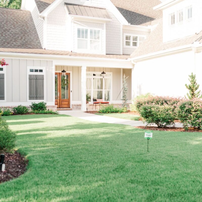 Lush green lawn in front of a two-story whilte house with a porch and a Nature's Turf sign in the middle of the lawn