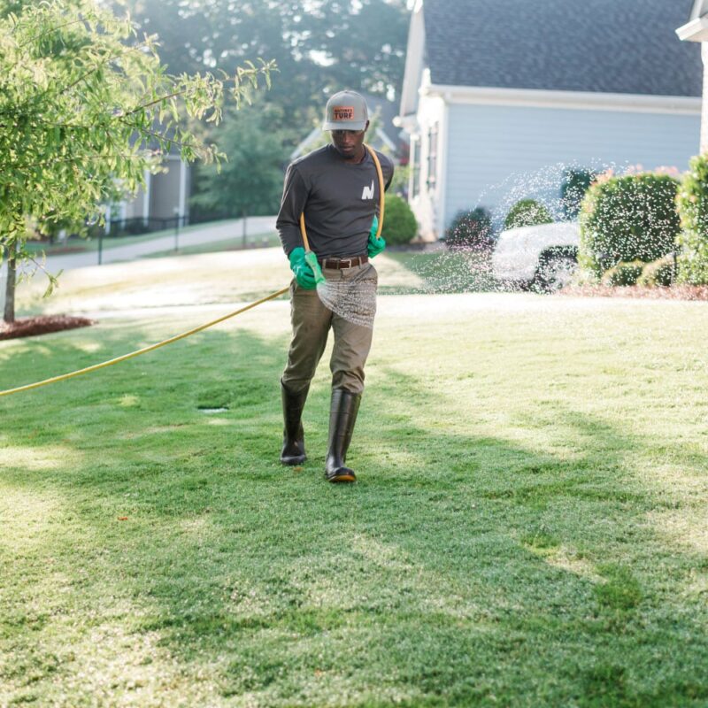 Nature's Turf employee applying weed control products to a lush green lawn through a hose