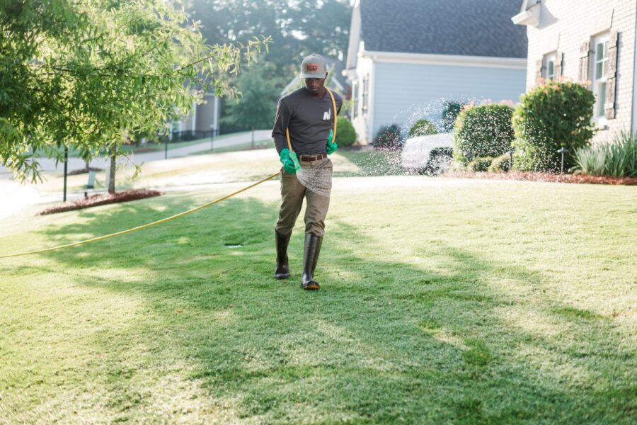 Nature's Turf employee applying weed control products to a lush green lawn through a hose