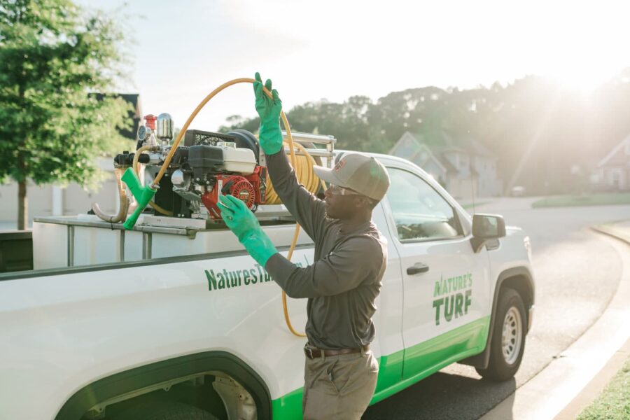 Nature's Turf employee pulling a lawn product applicator hose from a company truck parked on the street next to a curb