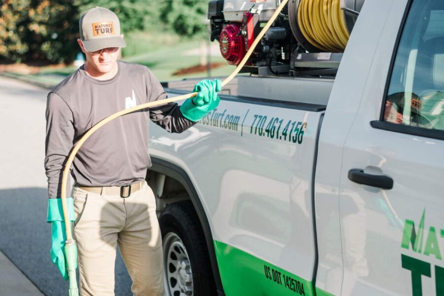 Nature's Turf employee standing between a street curb and the Nature's Turf truck and holding a weed control product applicator hose