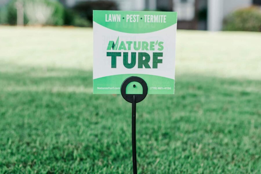 Nature's Turf yard sign stuck in the middle of a lush green lawn with a big white house in the background