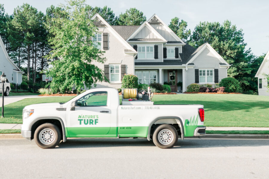 Nature's Turf truck parked on the street in front of a white house with a beautiful lawn