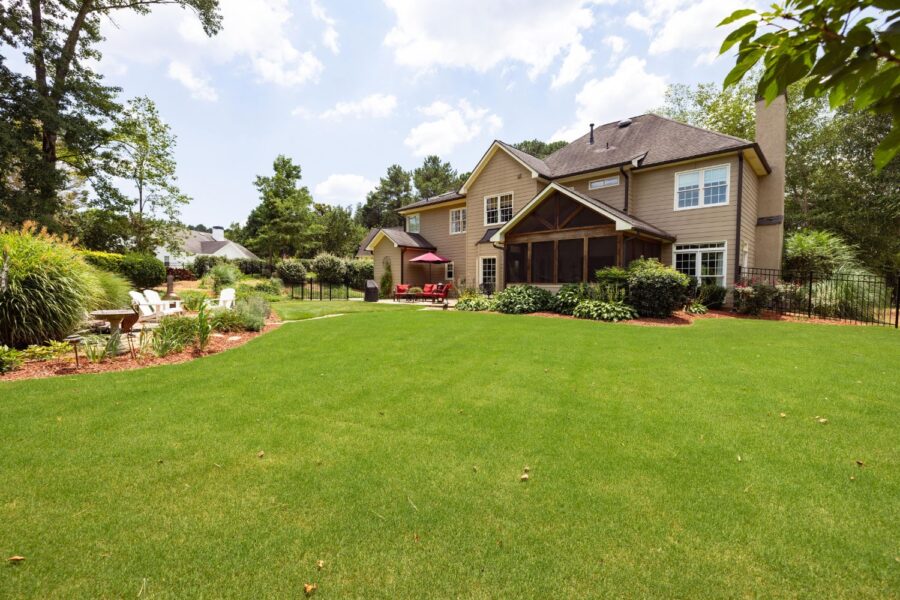 Two-story brown house with dark wood accents and a screened porch with a beautifully manicured lawn